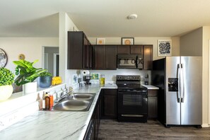 A modern kitchen with dark cabinets, stainless steel appliances, a marble countertop, and a potted plant. - Fabulous 3-bedroom house with AC in charming Conway (Conway)