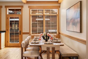 A dining room with a long table set for six, wooden chairs, a vase with flowers, and a painting on the wall. - Big Sky Getaway | Fireplace + Shared Pool + Grill (Big Sky)