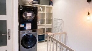 Un espace buanderie comprenant un lave-linge et un sèche-linge, une étagère blanche et un luminaire.