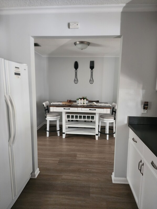 A kitchen with a white refrigerator, a dining table with chairs, and a black countertop. - The Relax spot
golf, hospital, restaurants, raceway and shops near by. (Sebring)