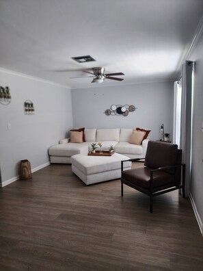 A living room with a sectional sofa, a brown leather chair, a ceiling fan, and a wall-mounted decor piece. - The Relax spot
golf, hospital, restaurants, raceway and shops near by. (Sebring)