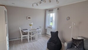 A room with a dining table and chairs, a black bean bag, a grey sofa, and a window with curtains. - Lyckeby Lodge – A Quiet Apartment Near Nature, Sea & City (Lyckeby)