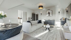 Ein modernes Wohnzimmer mit einem grauen Sofa, einem runden Couchtisch und einem Essbereich mit Tisch für zwei Personen.