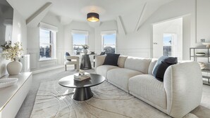 Ein geräumiges Wohnzimmer mit einer großen Couch, einem Couchtisch und Blick auf die Stadt durch große Fenster.