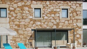 Een stenen gebouw met een zwembad, ligstoelen en een overdekt zitgedeelte.