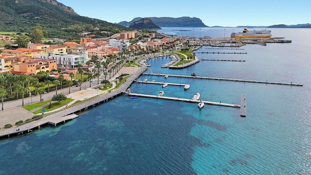 Eine Küstenstadt mit einem Yachthafen, Gebäuden entlang der Uferlinie und einem Berg im Hintergrund.