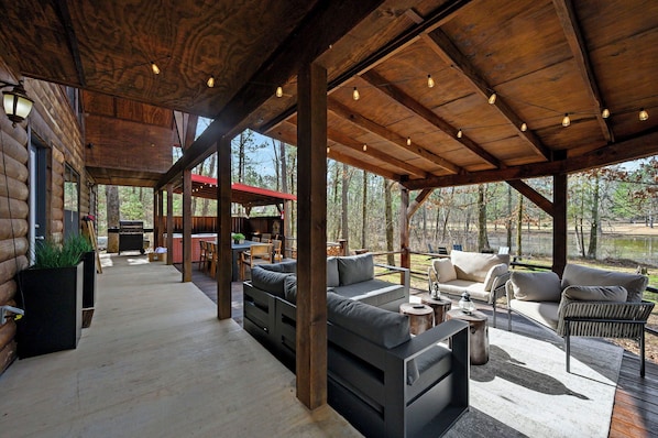 A covered outdoor area with a wooden ceiling, built-in seating, and a view of the surrounding forest. - Waterfront Cabin • Pond • Hot Tub • Great Location (Broken Bow)