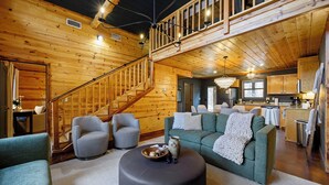 A spacious living area with a staircase, a green sofa, and a round ottoman. - Waterfront Cabin • Pond • Hot Tub • Great Location (Broken Bow)