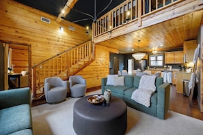 A spacious living area with a staircase, a green sofa, and a round ottoman. - Waterfront Cabin • Pond • Hot Tub • Great Location (Broken Bow)