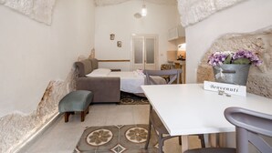 Una habitación acogedora con una cama, una mesita con un letrero, una silla y una maceta decorativa.