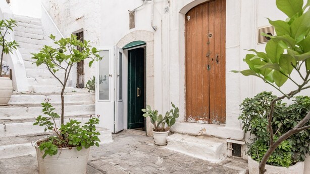 Una calle estrecha con edificios blancos, una puerta de madera y macetas con plantas.