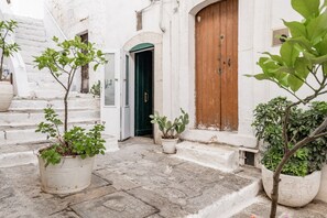 Una calle estrecha con edificios blancos, una puerta de madera y macetas con plantas.