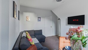 Ein modernes Wohnzimmer mit einem grauen Sofa, einem an der Wand montierten Fernseher und einer Tür zu einem anderen Raum.