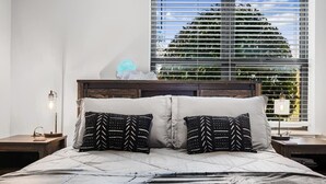 Ein Schlafzimmer mit einem großen Bett, zwei Nachttischen, einem Neonzeichen und einem Fenster mit Jalousien.