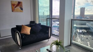 A modern office space with a black sofa, a glass coffee table, and a view of a cityscape through large windows. - NewStreet 1Bed Birmingham with Self Checkin (Birmingham)