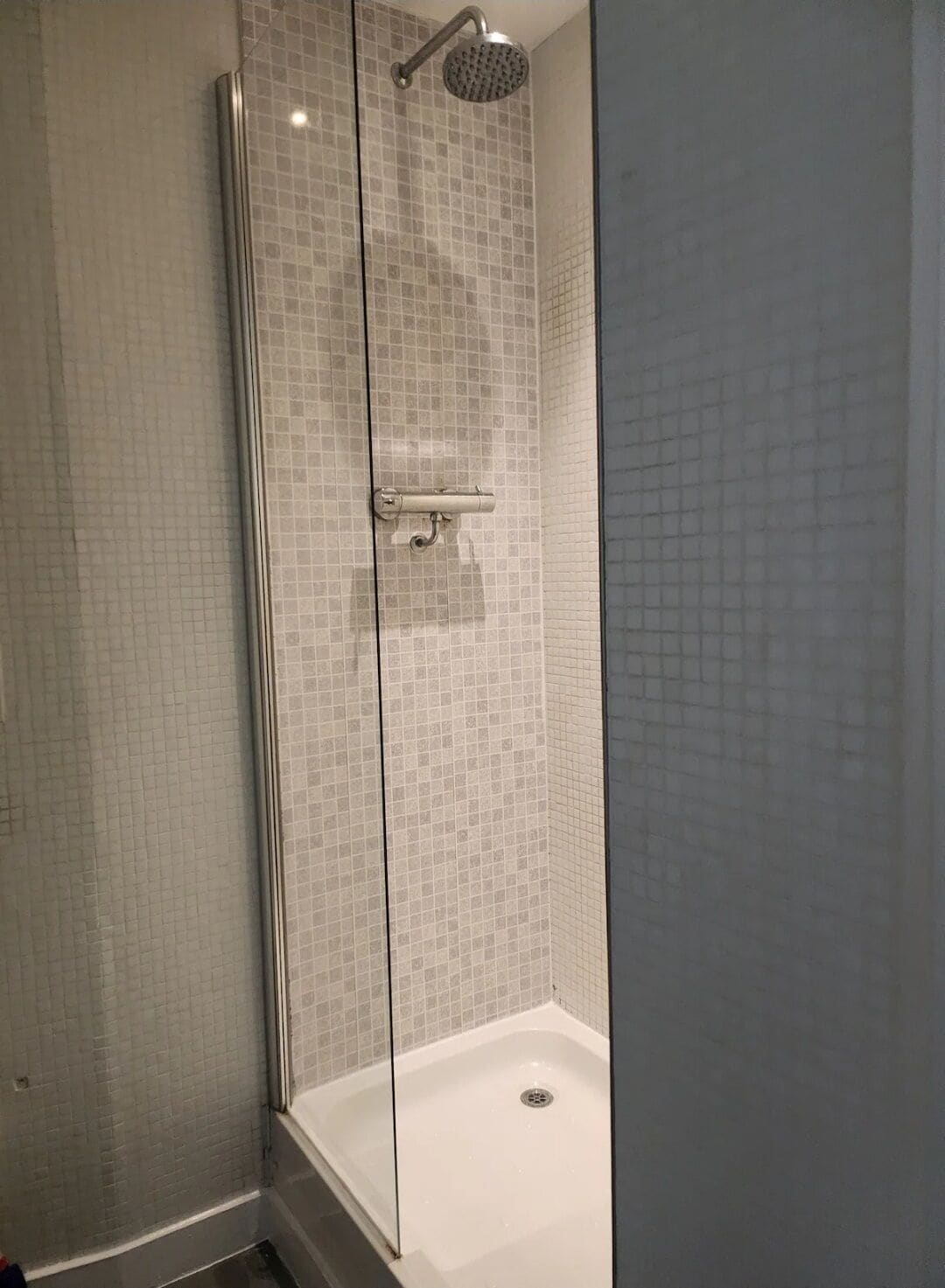 En dusch med glasväggar, en vägg beklädd med kakel och ett vitt badkar.