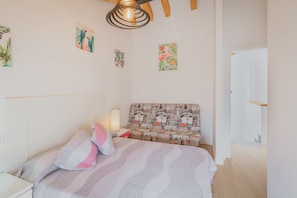 Un dormitorio con cama, mesita de noche, lámpara, banco con asiento estampado y decoración en la pared.