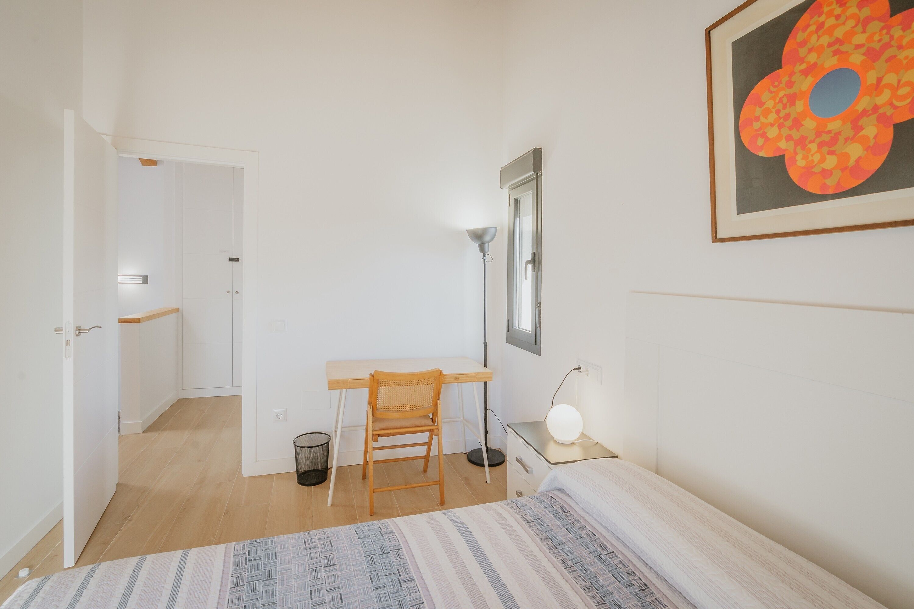 Une chambre à coucher avec un lit, un bureau, une chaise, une lampe et un tableau encadré au mur.