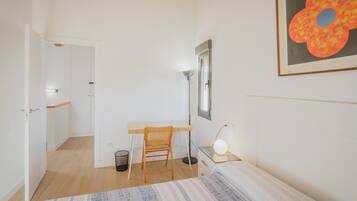 Ein Schlafzimmer mit Bett, Schreibtisch, Stuhl, Lampe und einem gerahmten Bild an der Wand.