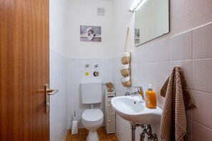 A bathroom with a toilet, sink, and a towel hanging on the wall. - 2-room first floor apartment with terrace 4 (Oberaudorf)