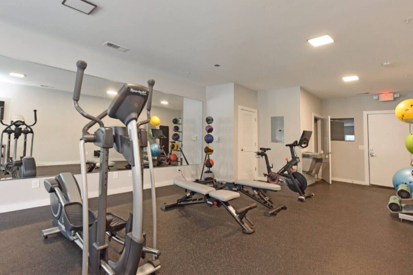Une salle de sport équipée de divers appareils d’exercice, notamment un vélo d’appartement, un appareil elliptique et des machines de musculation.