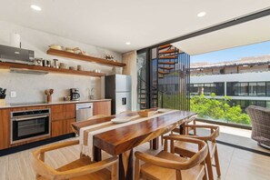 Une cuisine moderne avec des meubles en bois, des appareils en acier inoxydable et un coin repas comprenant une table et des chaises en bois.