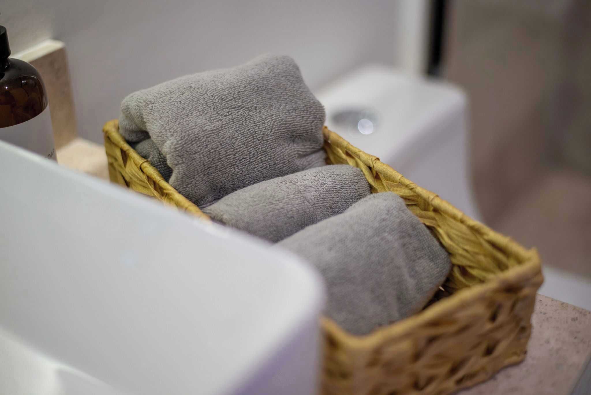 Un baño con una cesta de mimbre que contiene tres toallas, una bañera blanca y un inodoro blanco.