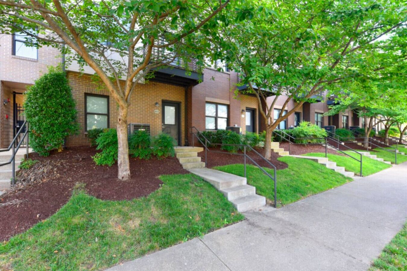 A residential building with brick exterior, multiple windows, and a well-maintained lawn with trees.