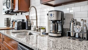 Une cuisine dotée de plans de travail en granit, d’une machine à café, d’un grille-pain et d’un bloc à couteaux.
