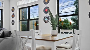 Un espace repas moderne avec une table en bois, des chaises blanches et un canapé gris. On peut voir des disques vinyle accrochés au mur et une plante posée sur la table.