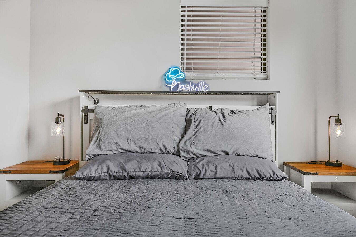 A bedroom with a bed, two bedside tables, a headboard, and a window with blinds.