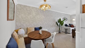 Een moderne woonkamer met een ronde houten eettafel, witte stoelen, een bank met kussens, een potplant en een bijzondere plafondlamp.