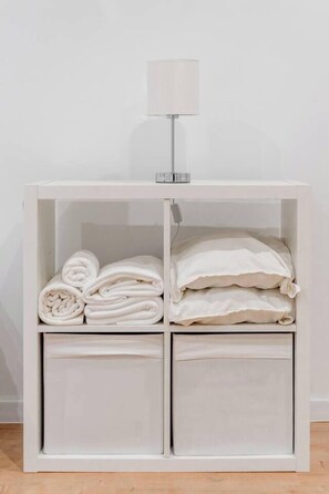 A white bedside table with a lamp, a folded towel, and a rolled-up towel. - Podgórze Apartment - 54m2, Air Con - by Rentujemy (Kraków)