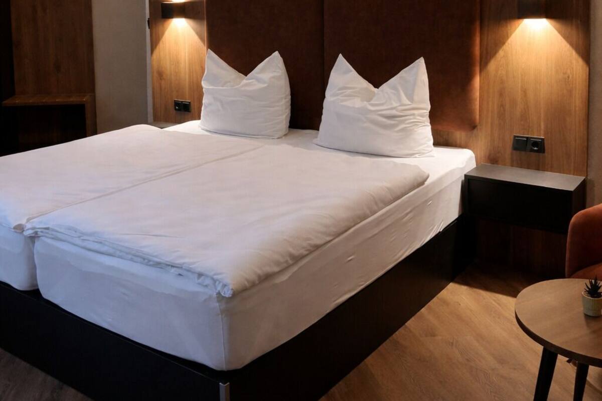 Una habitación de hotel moderna con una cama grande, cabecera de madera, lámparas de noche y una pequeña mesa.