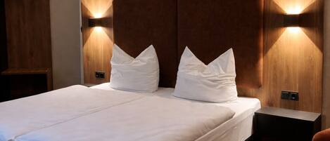 Una habitación de hotel moderna con una cama grande, cabecera de madera, lámparas de noche y una pequeña mesa.