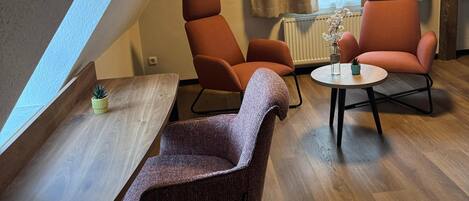 Un dormitorio tipo loft moderno con techo inclinado, dos sillones naranjas, una mesita redonda y una planta en maceta.