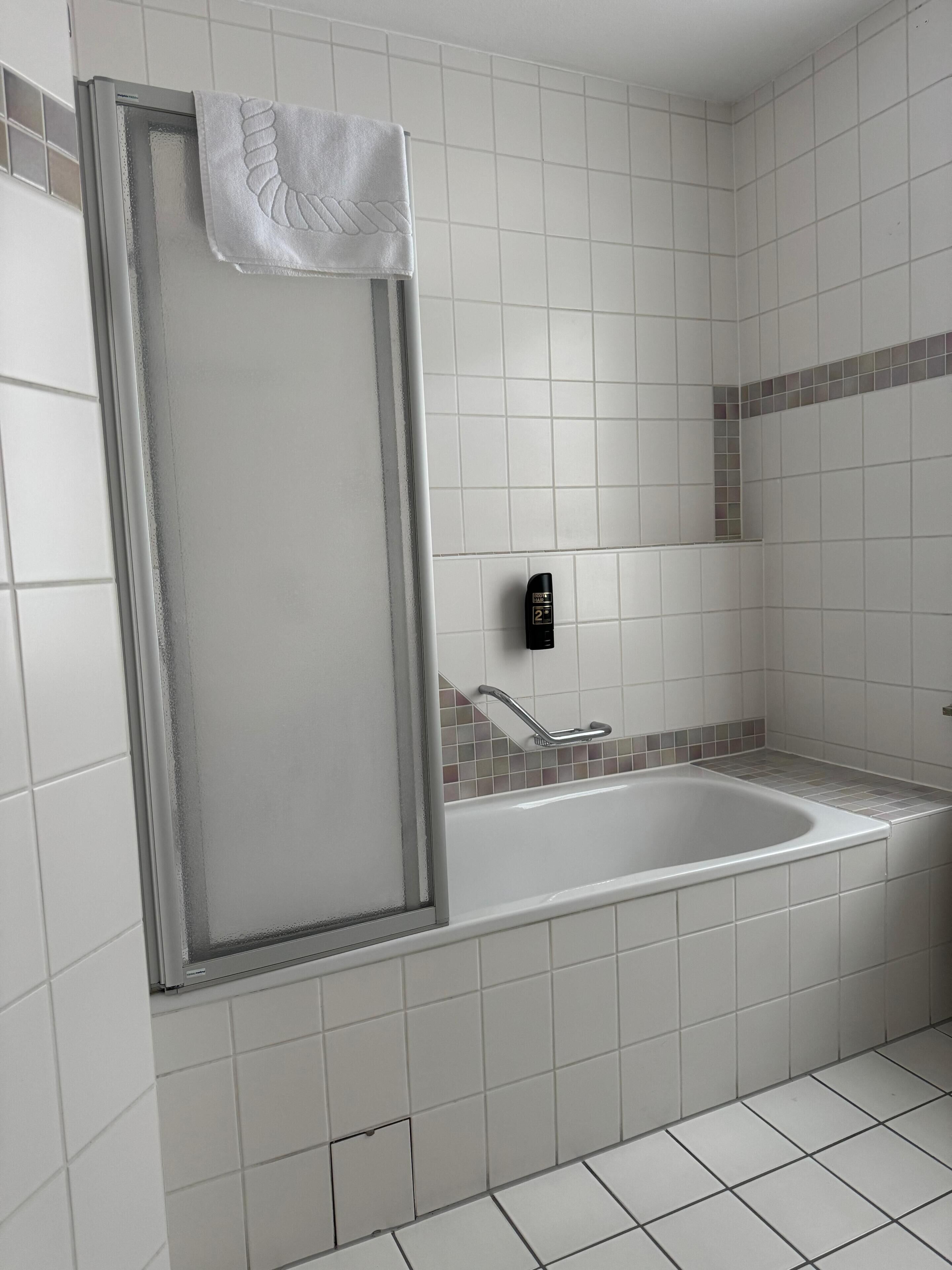 Bagno con cabina doccia, vasca, mancorrente e pannello comandi a parete.