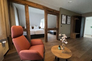 Quarto moderno com uma janela grande, cama com estrutura de madeira, uma cadeira vermelha, uma mesa pequena com um vaso e um banco de madeira.