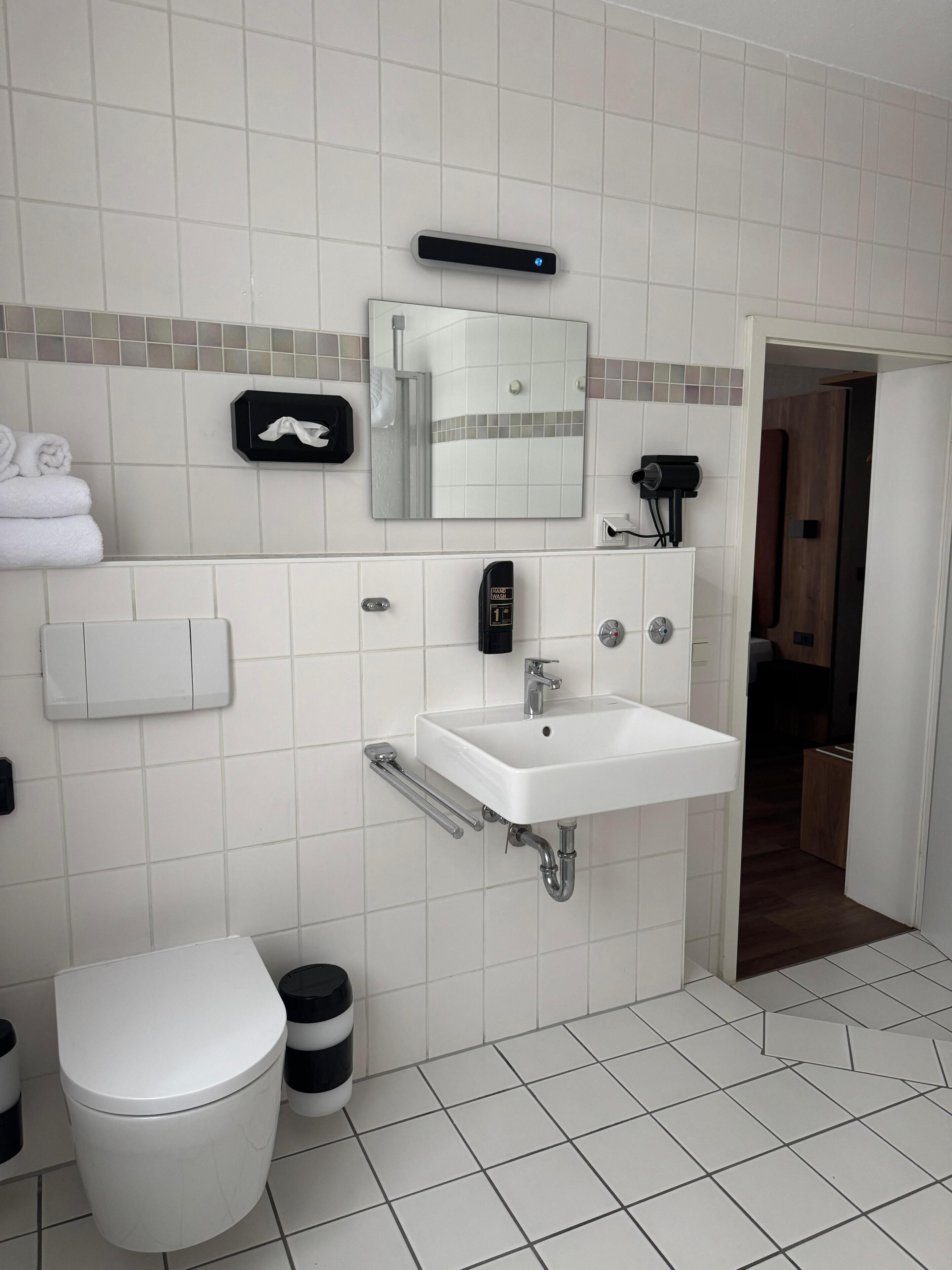 Ein modernes Badezimmer mit einem weißen Waschbecken, einem Spiegel, einem Handtrockner und einer Toilette.
