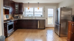 Una cocina moderna con armarios de madera oscura, electrodomésticos de acero inoxidable y vistas al agua a través de amplios ventanales.