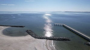 Una playa con un muelle de hormigón que se adentra en aguas tranquilas, rodeada por un rompeolas rocoso.