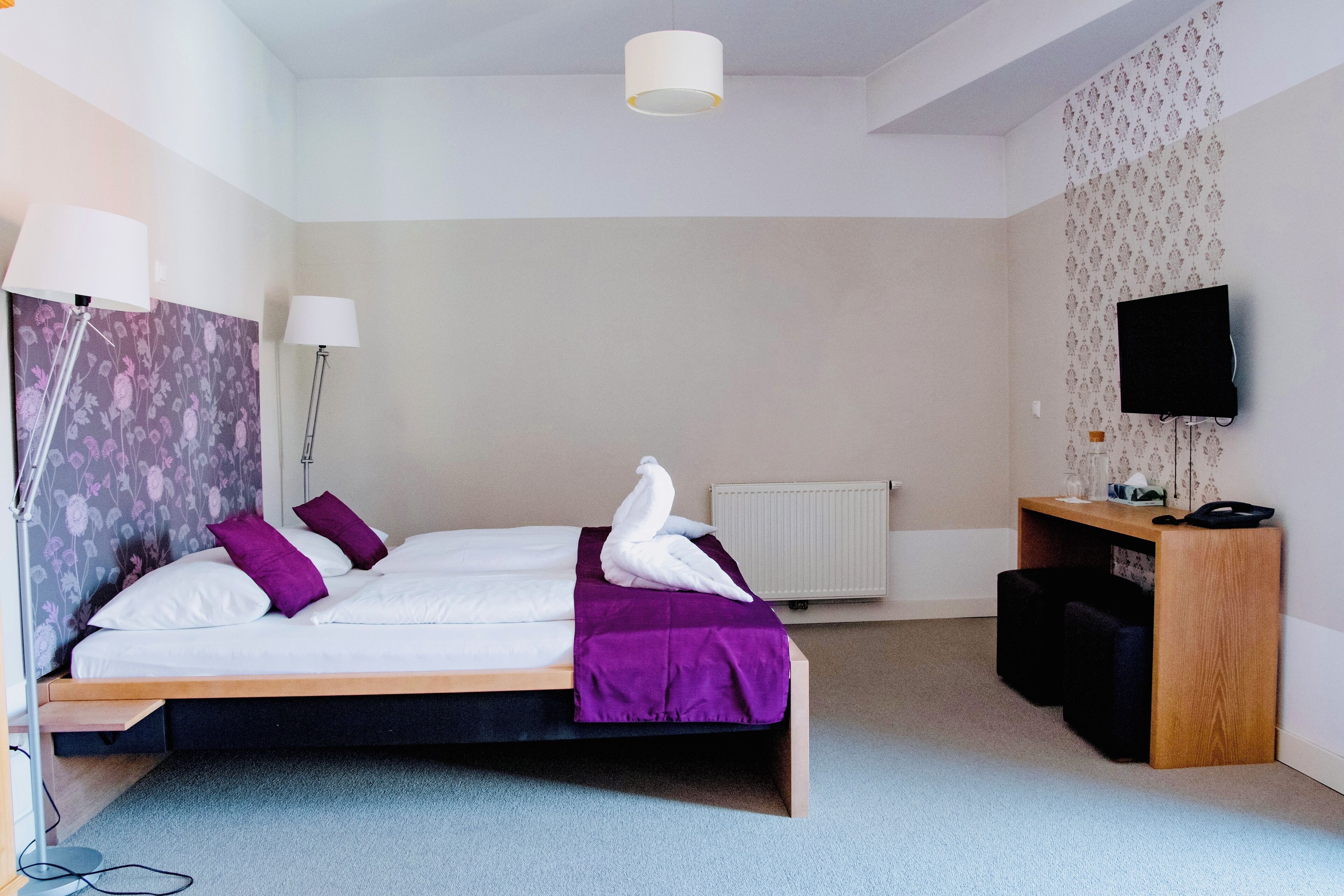 A modern hotel room with a bed, a desk, a television, and a radiator.