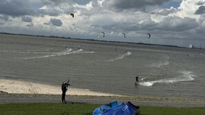 A beach with people windsurfing and kitesurfing, a clear sky, and a distant city skyline. - Vacation apartment Puustpaus close to the beach (Butjadingen)