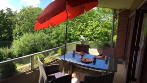 A balcony with wicker furniture, a table with food, and a red umbrella. - Vacation apartment Puustpaus close to the beach (Butjadingen)