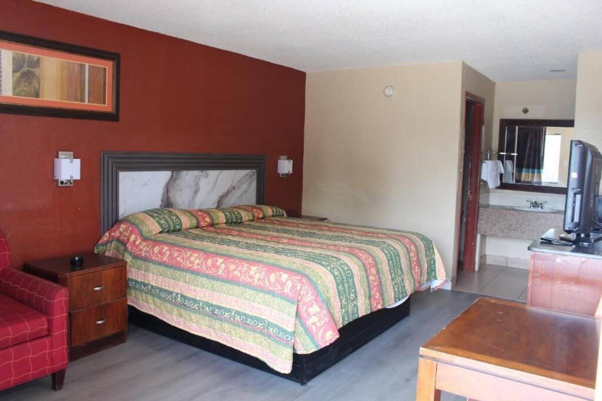 A hotel room with a bed, a desk, a chair, a television, and a bathroom visible through an open door.