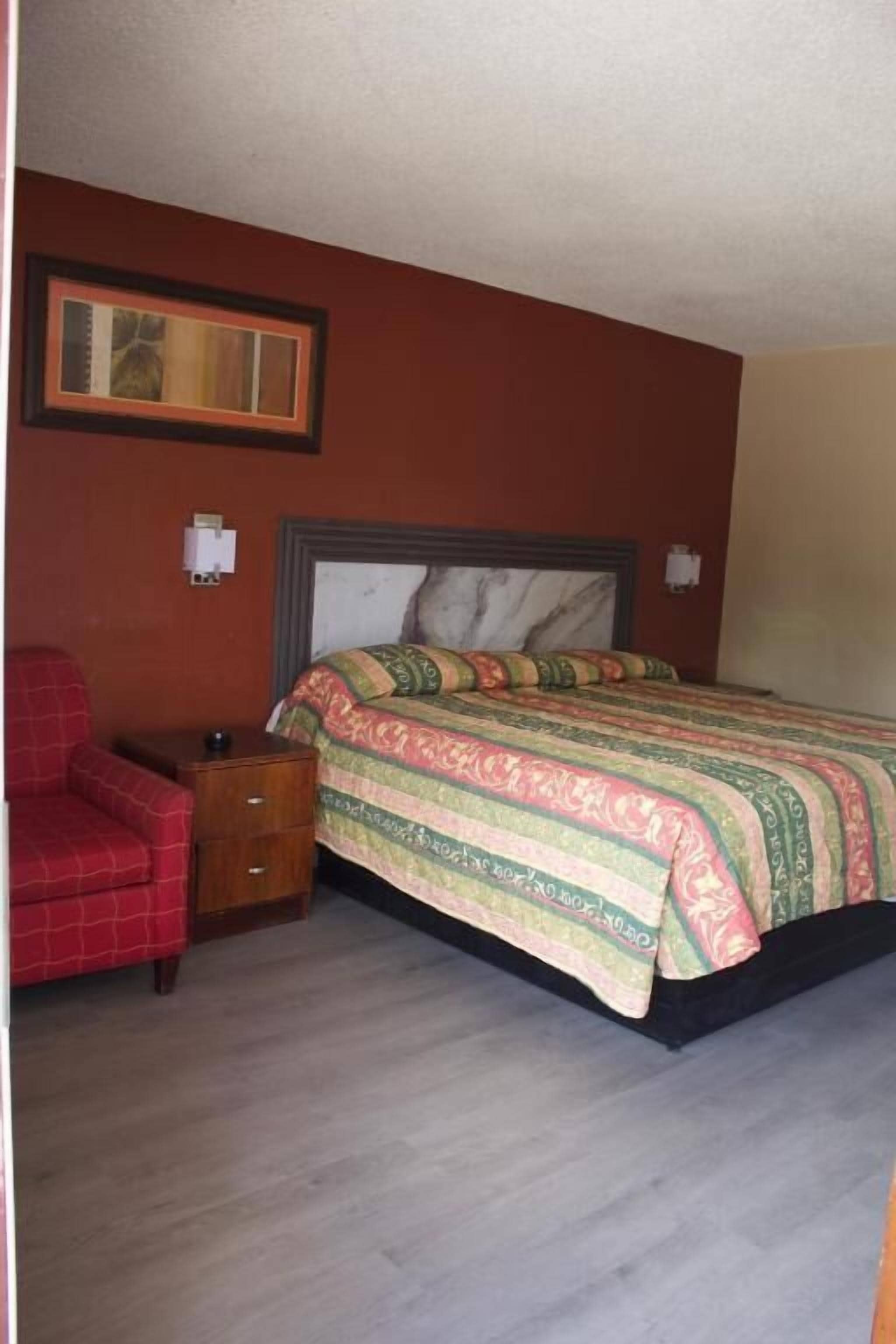 A bedroom with a bed, a chair, a nightstand, and a framed picture on the wall.