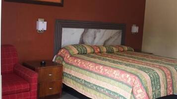 A bedroom with a bed, a chair, a nightstand, and a framed picture on the wall.