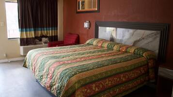A bedroom with a large bed, a red chair, a window with curtains, and a framed picture on the wall.