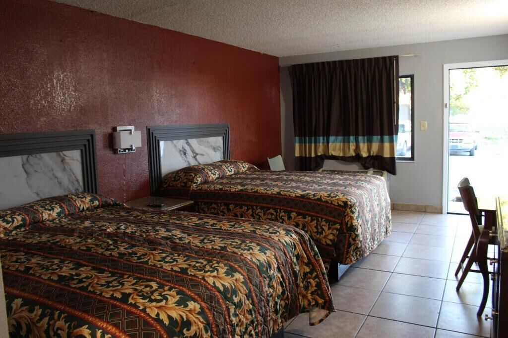 A hotel room with two beds, a red wall, a window with curtains, and a view of the outside.