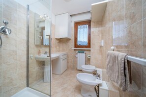 A bathroom with a shower, sink, toilet, and a window with a curtain. - GuestHost - Charming studio in Tarvisio, ideal for 3 people, equipped with a balcony offering breathtaking views of the Alps. The accommodation is perfect for a romantic getaway or a nature adventure. Tarvisio is a paradise for winter sports enthusiasts  (Tarvisio)